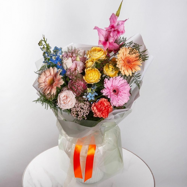 Gerbera daisies - 2, Pink Gladiolus - 1, Pink carnation - 5, Peony sprayrose - 1, Spray rose: yellow, orange 50 cm - 1, Gerbera pink - 3, Pink Lisianthus (Eustoma) - 1, Cream gerbera - 2, Blue Delphinium, Asparagus setaceus (1 pc.), Wrapping Paper